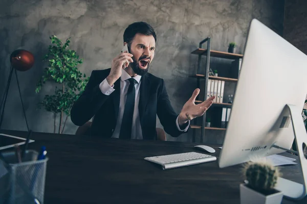 Foto de hombre barbudo agresivo enojado sentarse escritorio hablar teléfono mirar pantalla pc usar traje camisa corbata en la oficina moderna en interiores —  Fotos de Stock