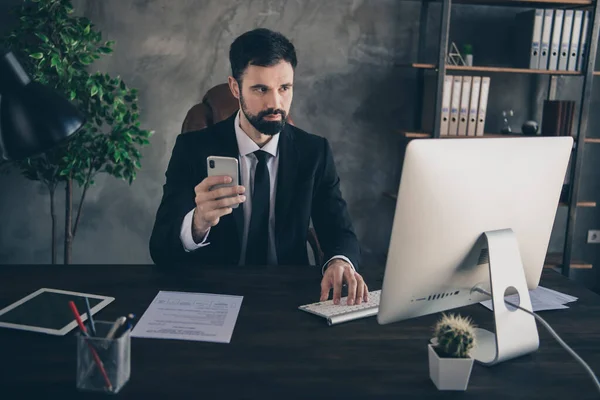 Foto van agent ceo bebaarde man zit bureau pc houden telefoon dragen formele pak shirt stropdas in modern kantoor binnen — Stockfoto