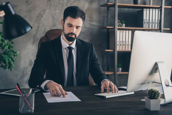 Fénykép koncentrált ügynök férfi ül íróasztal számítógép gépelés tapintás papír viselet formális öltöny ing nyakkendő modern irodai beltérben — Stock Fotó