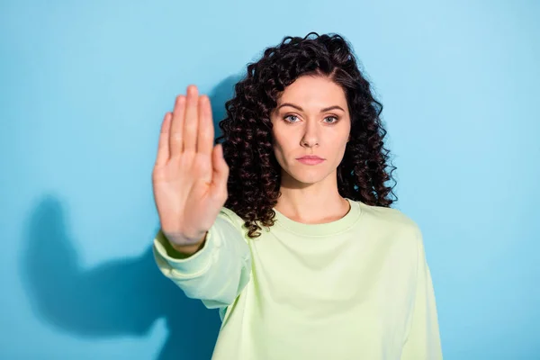Foto de mujer morena confiada levantar la prohibición de la mano signo de desgaste sudadera verde aislado fondo azul —  Fotos de Stock