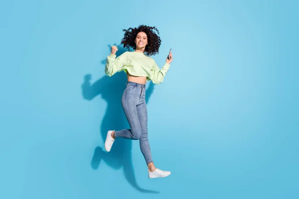 Full längd foto av glad person knytnäve upp fira hoppa högt strålande leende isolerad på blå färg bakgrund — Stockfoto
