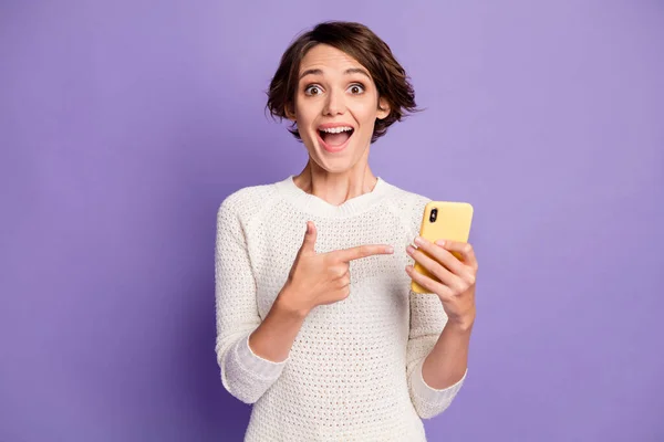 Фотопортрет дівчини з боб-волоссям, спрямованим пальцем на смартфон, посміхаючись ізольовано на яскраво-фіолетовому кольоровому фоні — стокове фото