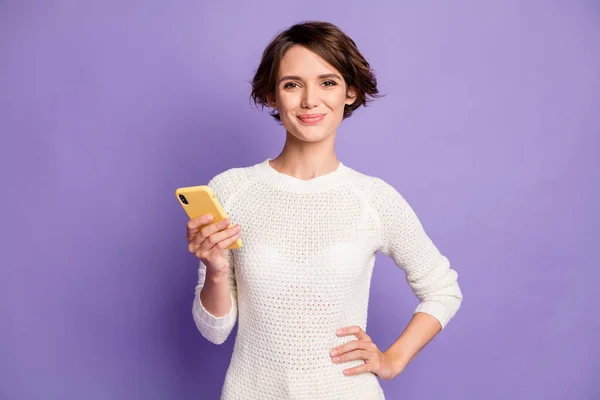 Retrato fotográfico de una estudiante bastante femenina mostrando cómo mantener el teléfono inteligente sonriendo aislado sobre un fondo de color violeta brillante —  Fotos de Stock
