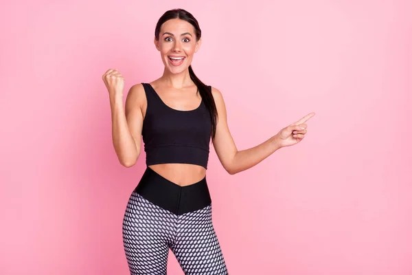 Photo of happy cheerful young woman point finger empty space raise fist win isolated on pink color background — Stock Photo, Image