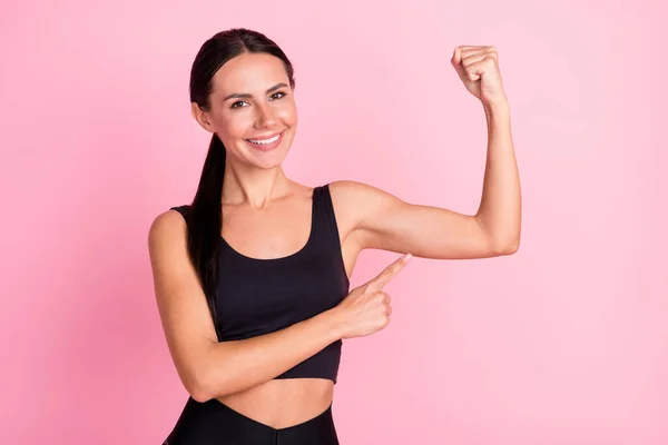 Foto de una encantadora mujer joven vestida con ropa deportiva que muestra los músculos del brazo del dedo que señalan sonriendo aislado color rosa fondo —  Fotos de Stock