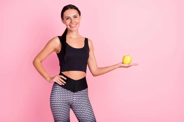Foto de una joven bastante alegre vestida con ropa deportiva sosteniendo el brazo de la mano manzana verde sonriendo aislado color rosa fondo —  Fotos de Stock