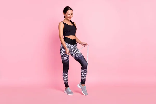 Foto de positivo bastante joven ropa deportiva medida pierna cinta sonriente aislado color rosa fondo —  Fotos de Stock
