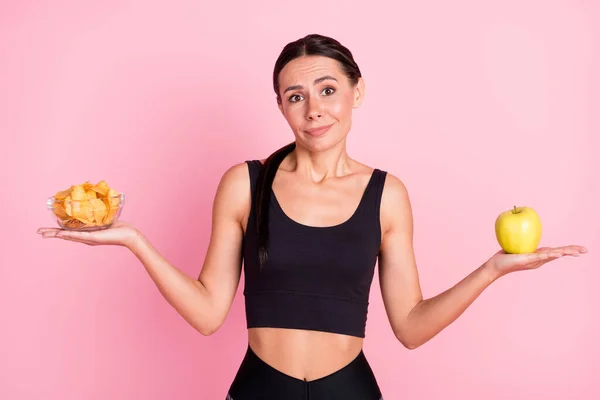 Photo de faim douteuse jeune dame vêtements de sport décider ce que manger croustilles pomme verte isolé couleur rose fond — Photo