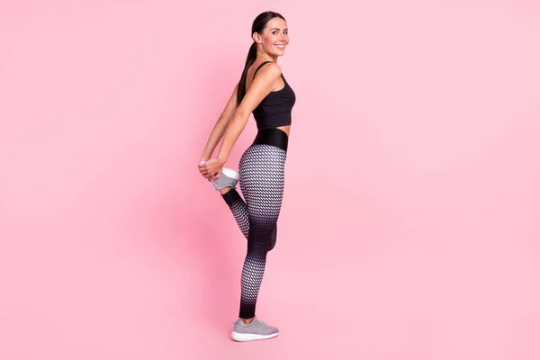 Foto von selbstbewusst entzückende junge Frau gekleidet sportliches Outfit lächelnd Stretching isoliert rosa Farbe Hintergrund — Stockfoto