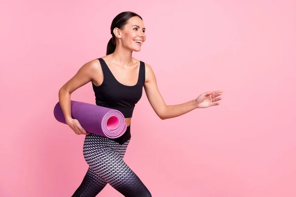 Foto de adorable joven bonita ropa deportiva corriendo rápido celebración estera de yoga buscando espacio vacío aislado color rosa fondo —  Fotos de Stock