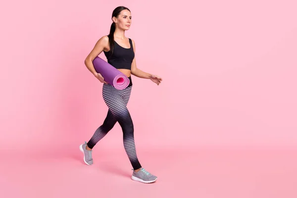 Foto de bastante encantadora joven ropa deportiva corriendo rápido sosteniendo estera de yoga buscando espacio vacío aislado color rosa fondo —  Fotos de Stock