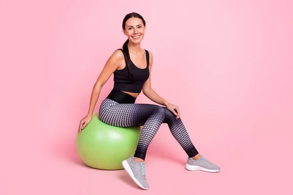 Foto de bonito jovem senhora sportswear tendo descanso grande bola verde apto sorrindo isolado cor de fundo rosa — Fotografia de Stock