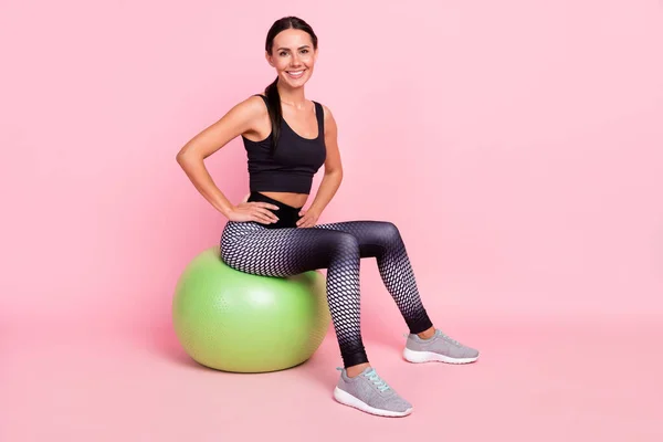 Foto de linda adorable joven mujer vestida traje deportivo sonriendo teniendo descanso verde fitball brazos cintura aislado color rosa fondo —  Fotos de Stock