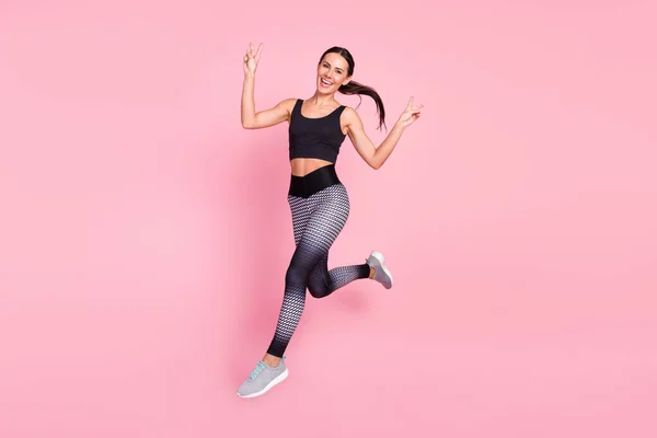 Full kropp profil sida foto av ung sportig kvinna glad leende springa hoppa visa fred cool v-tecken isolerad över pastell färg bakgrund — Stockfoto