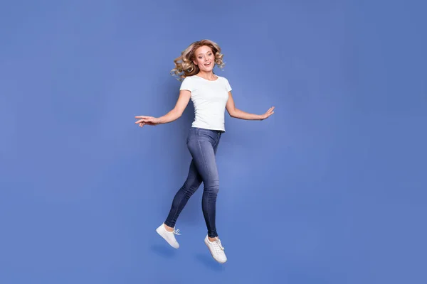 Lunghezza completa dimensione del corpo vista di attraente allegra ragazza dai capelli ondulati salto a piedi buon umore isolato su sfondo di colore blu — Foto Stock