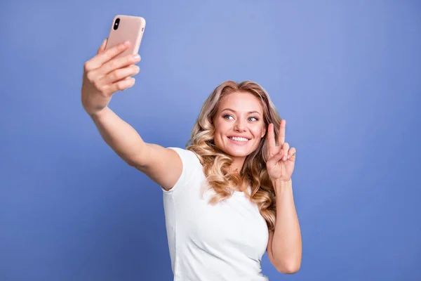 Portrét atraktivní veselý vlnité-vlasy dívka přičemž selfie ukazující V-znak izolované přes modré barvy pozadí — Stock fotografie