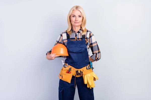 Photo of charming confident mature handywoman workwear holding hard hat isolated grey color background — Stock Photo, Image