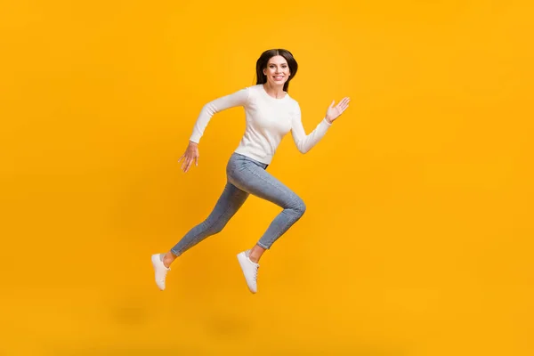 Foto de perfil em tamanho real de menina otimista salto corrida desgaste camisola jeans tênis isolado no fundo de cor amarela — Fotografia de Stock