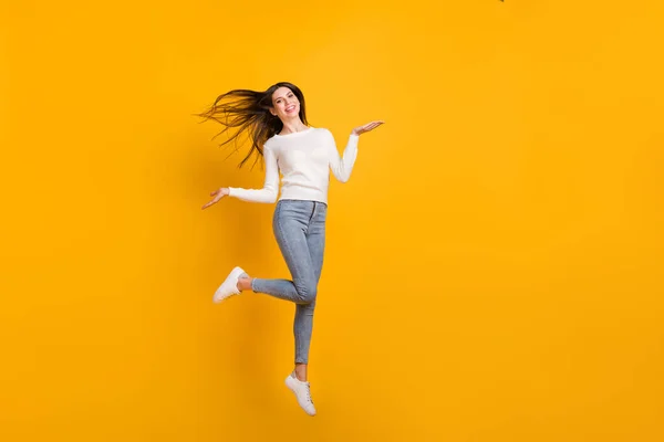 Фотографія оптимістичної дівчини, що стрибає, носить светр джинси кросівки ізольовані на жовтому кольоровому фоні — стокове фото