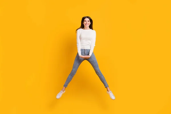 Foto em tamanho completo de otimista bonito menina salto desgaste camisola jeans tênis isolado no fundo de cor amarela — Fotografia de Stock