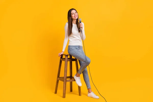 Foto em tamanho completo de menina agradável otimista sentar cantar no microfone desgaste camisola jeans tênis isolado no fundo de cor amarela — Fotografia de Stock