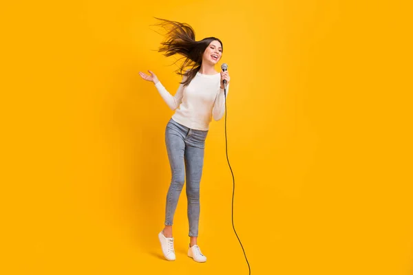 Mikrofon içinde şarkı söyleyen iyimser bir kızın tam boy fotoğrafı sarı arka planda izole edilmiş kazak kotları giyiyor. — Stok fotoğraf