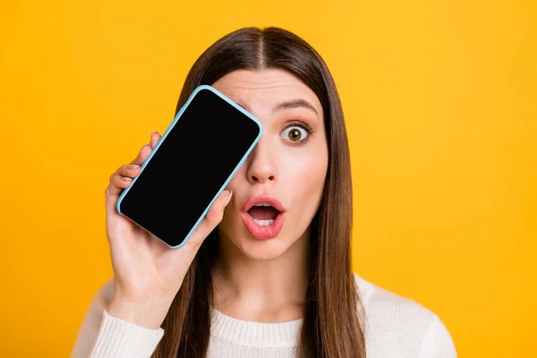Фото враженої брюнетки дівчина показує телефон в білому светрі ізольовані на жовтому кольорі — стокове фото