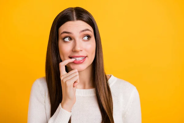 Foto de adorável pessoa positiva mordendo unha do dedo olhar espaço vazio bom humor isolado no fundo de cor amarela — Fotografia de Stock