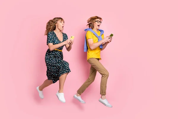 Profilo full size foto di coppia divertente ottimista salto sguardo telefono indossare vestiti colorati isolati su sfondo rosa pastello — Foto Stock