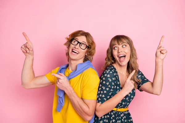 Foto de joven feliz sonriente funky divertida pareja señalando dedos copyspace anuncio aislado en el fondo de color rosa —  Fotos de Stock