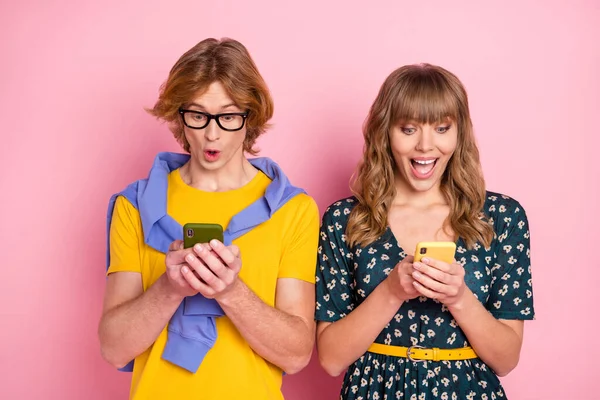 Foto di stupito giovane uomo e donna tenere telefono usura vestito giallo t-shirt pantaloni isolati su sfondo di colore rosa — Foto Stock