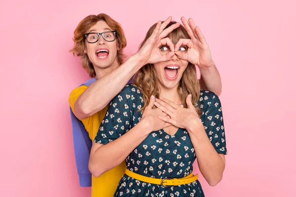 Fénykép az optimista szép pár show szemüveg viselni színes ruhák elszigetelt pasztell rózsaszín háttér — Stock Fotó
