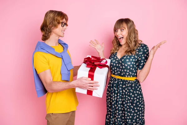 Portret van aantrekkelijke vrolijke paar met plezier guy geven giftbox naar verbaasd meisje gelegenheid geïsoleerd over roze pastel kleur achtergrond — Stockfoto