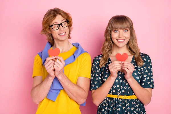 Foto van jong vrolijk glimlachend paar houden weinig rood papier harten Valentijnsdag geïsoleerd op roze kleur achtergrond — Stockfoto