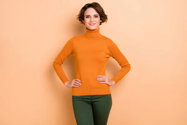 Foto de brillante joven bonita usar naranja cuello alto manos brazos cintura aislado color beige fondo — Foto de Stock