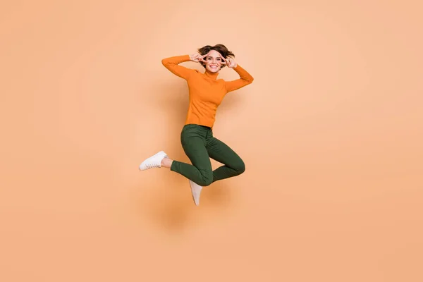 Foto em tamanho completo de jovem atraente adorável feliz sorridente alegre menina salto show v-sign isolado no fundo cor bege — Fotografia de Stock
