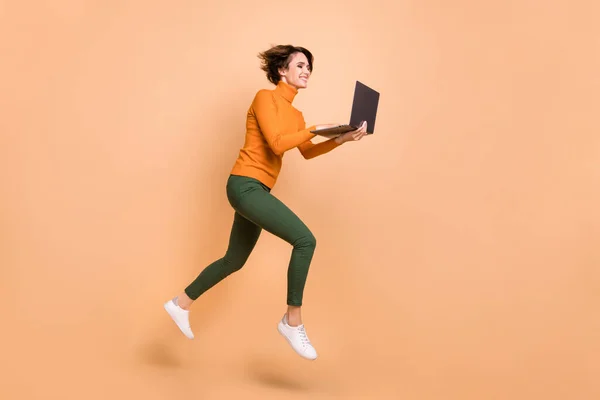 Foto de comprimento total de funky doce menina laranja gola alta comunicando gadget moderno saltando isolado cor bege fundo — Fotografia de Stock