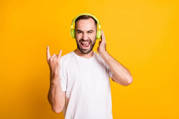 Retrato de tipo funky optimista escuchar música mostrar el signo de rock lengua fuera usar camiseta gris aislado sobre fondo de color amarillo —  Fotos de Stock