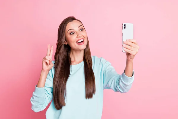 Foto de atractiva encantadora dama joven usar suéter azul mantenga el teléfono mostrar selfie v-signo aislado en el fondo de color rosa — Foto de Stock