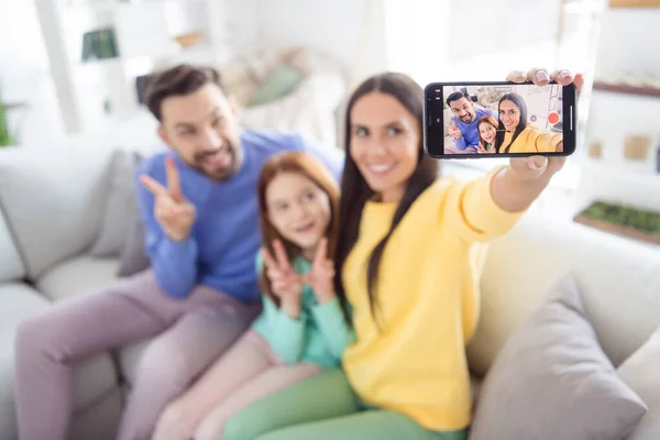 Foto de joven atractiva familia alegre feliz sonrisa positiva hacer selfie teléfono inteligente mostrar paz fresco v-signo sentarse sofá interior —  Fotos de Stock