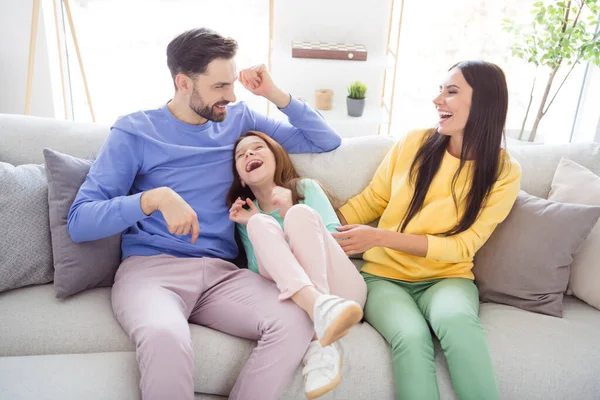 Photo of young cheerful family happy positive smile mom dad tickle daughter laugh have fun sit sofa home — Stock Photo, Image