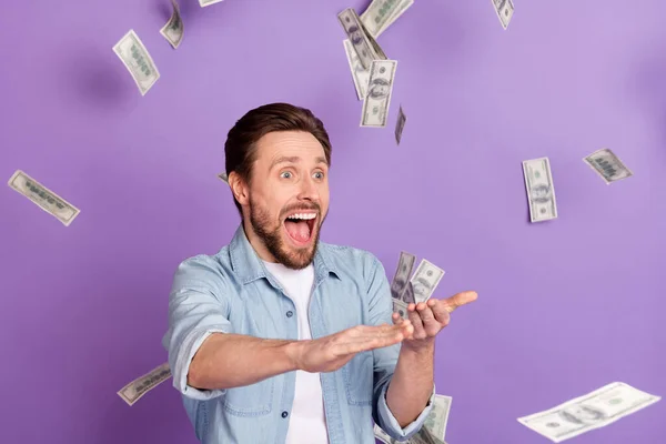 Foto von erstaunt fröhlich glücklich verrückter junger Mann fallen Geld reichen Reichtum fallen isoliert auf violetten Hintergrund — Stockfoto