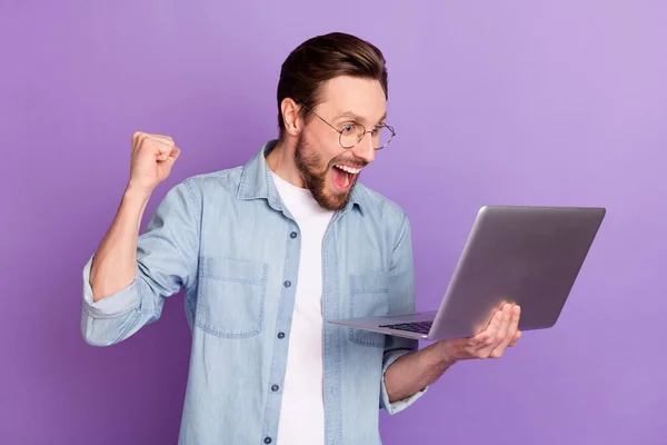 Foto van verbaasd opgewonden gelukkig jongeman verhogen vuist winnaar kijken laptop geïsoleerd op paarse kleur achtergrond — Stockfoto