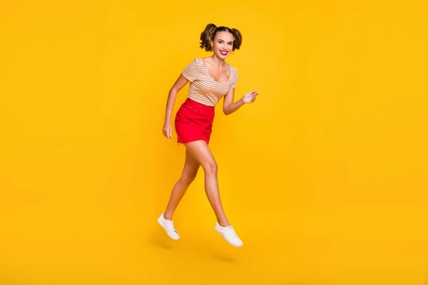 Foto de longitud completa de la muchacha con coletas salto ir llevar camiseta rayada falda corta zapatillas aisladas de color amarillo fondo —  Fotos de Stock