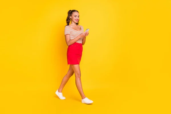 Full längd kroppsstorlek bild av attraktiv glad tunn fokuserad flicka med hjälp av enheten går isolerad över ljusa gula färg bakgrund — Stockfoto