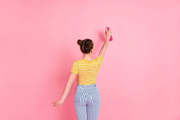 전반적 인 크기의 낙관적 이고 멋진 갈색 옷을 입은 여성의 뒷모습 페인팅 월 핑크 색 배경에 고립된 노란 티셔츠 바지를 입고 있다. — 스톡 사진