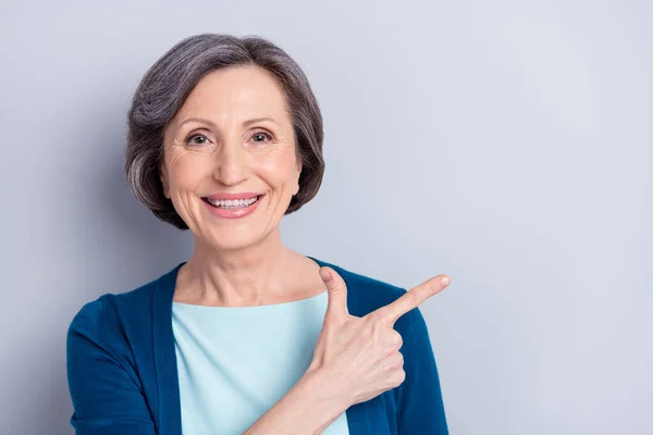 Foto retrato de sorrir mulher idosa feliz apontando espaço copyspace dedo recomendando isolado em fundo de cor cinza — Fotografia de Stock