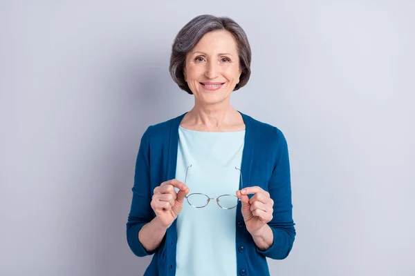 Φωτογραφία πορτρέτο της ηλικιωμένης επιχειρηματία χαμογελώντας κρατώντας τα γυαλιά απομονώνονται σε γκρι φόντο χρώμα — Φωτογραφία Αρχείου