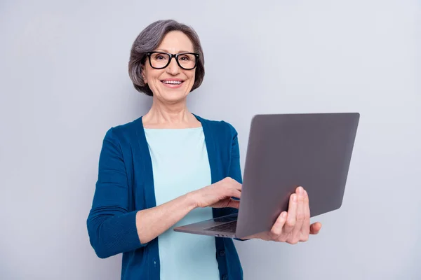 Photo de charmante belle belle vieille femme tenir les mains ordinateur portable sourire porter des lunettes isolées sur fond de couleur grise — Photo