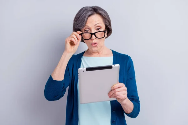 Foto retrato de empresária sênior vestindo óculos surpreendido leitura notícias no tablet isolado em fundo de cor cinza — Fotografia de Stock